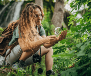 A woman in field gear crouched down examining a creature in her hand. She is a great example of someone who has a career working with wildlife.